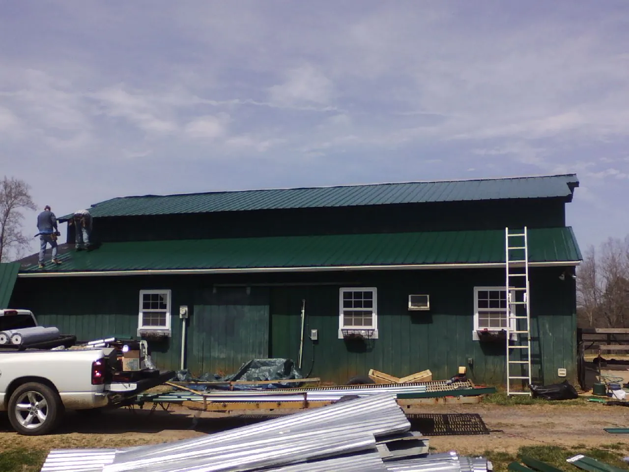 Crew installing green metal roofing on a large green barn in Berlin